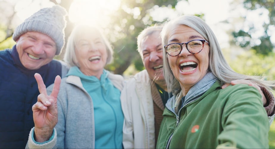 Fyra äldre grannar i en förening tar en glad selfie tillsammans utomhus i solen.